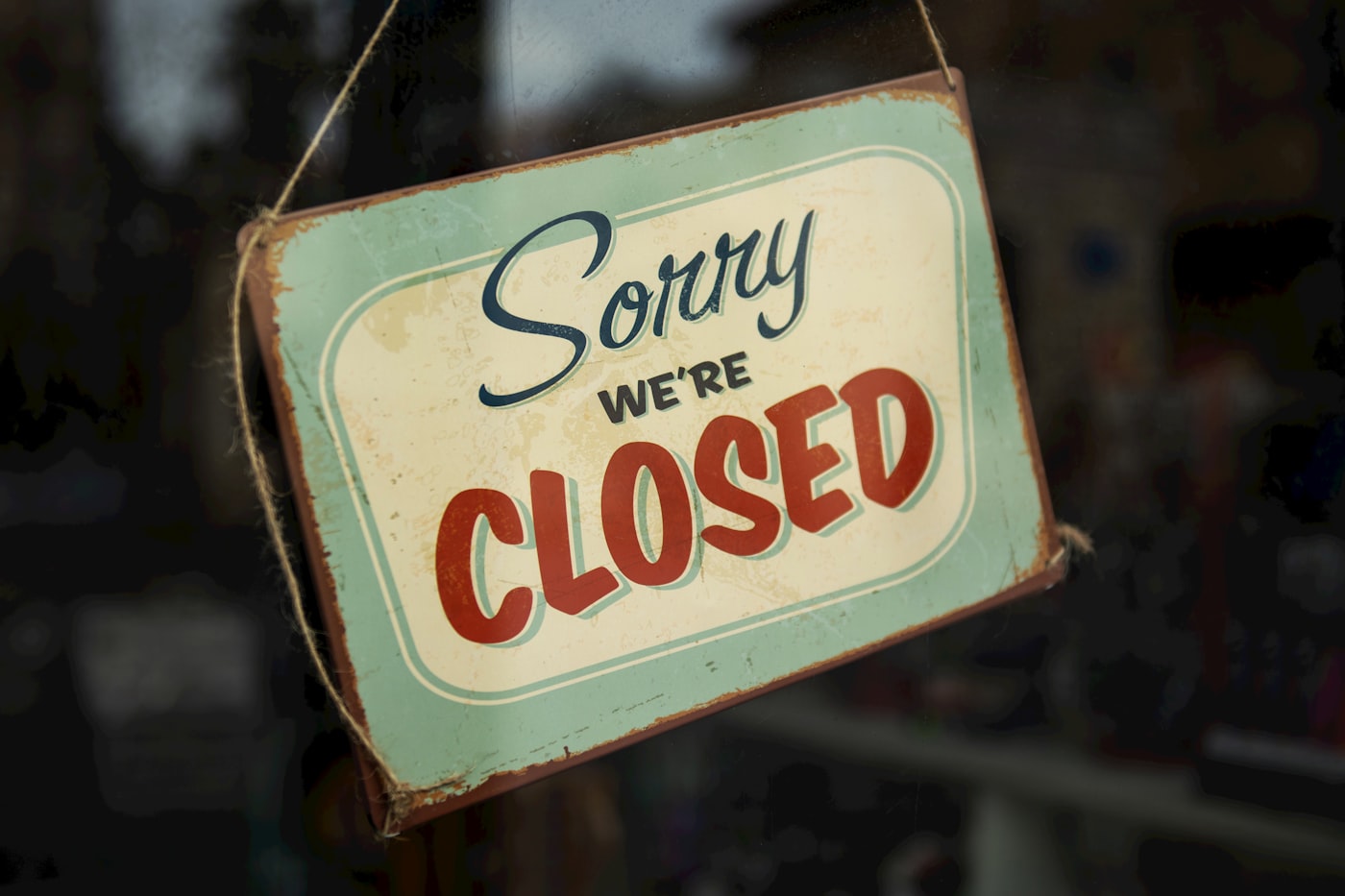 A sorry-we're-closed sign hanging in a dark shop window